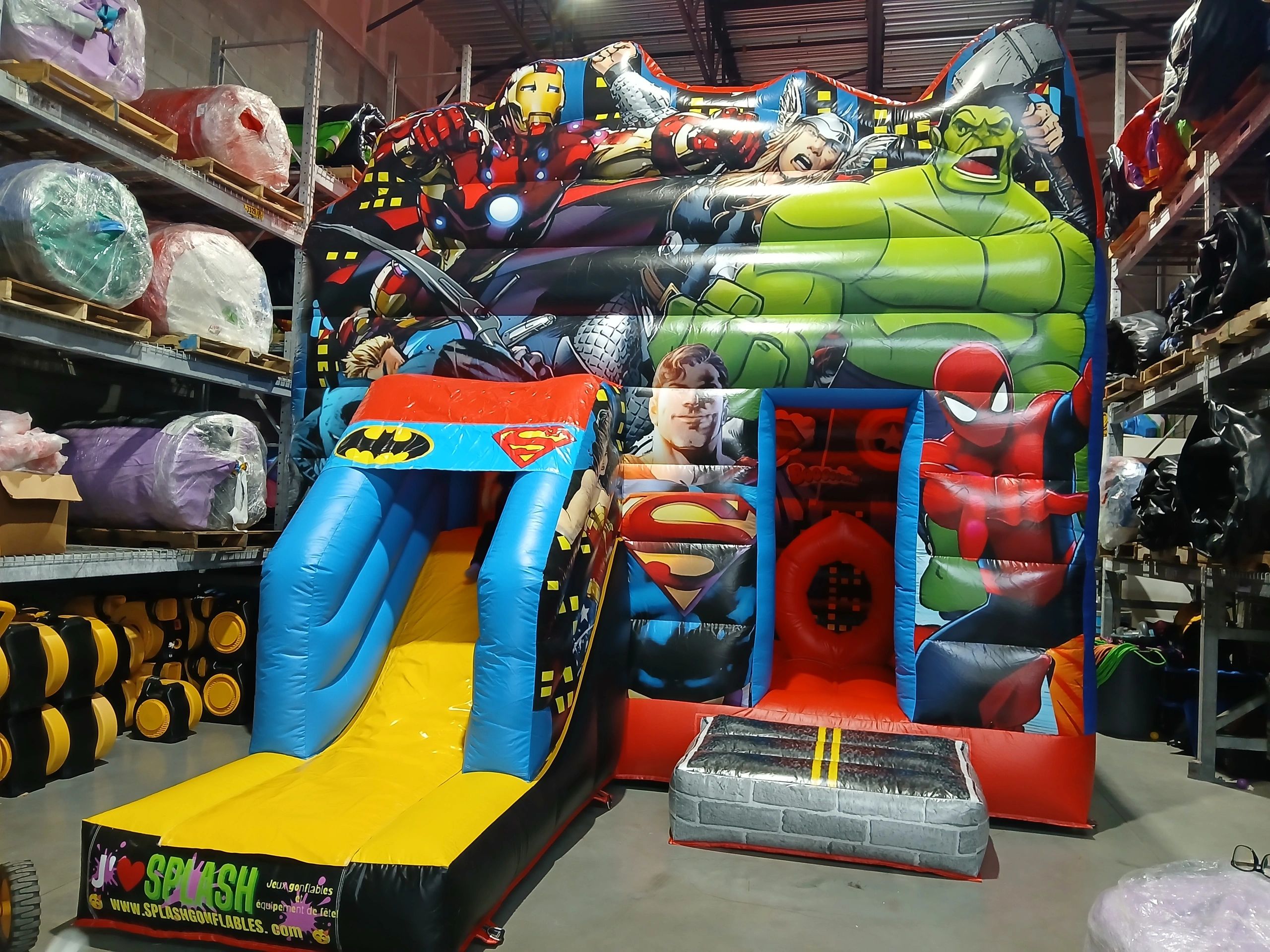 Colorful inflatable bounce house featuring various superheroes in a warehouse.