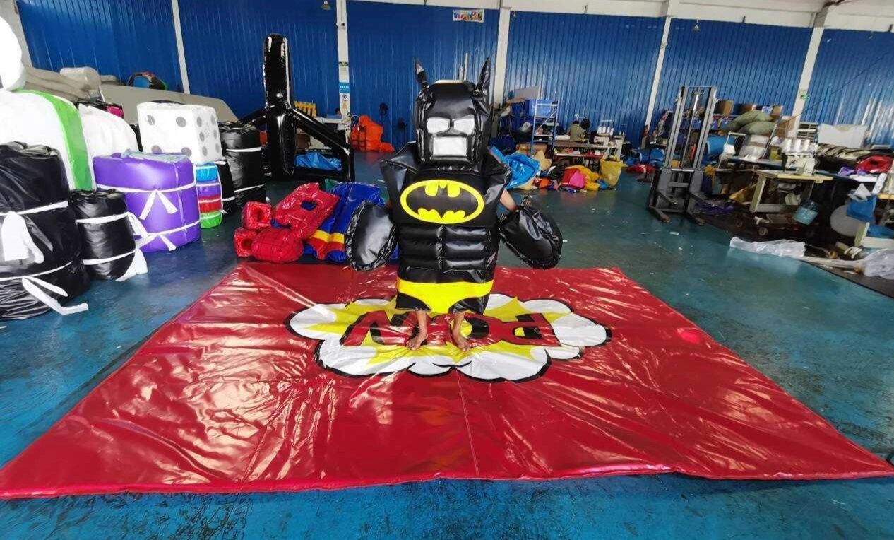 Inflatable Batman costume on a red mat with comic-style text in a workshop.