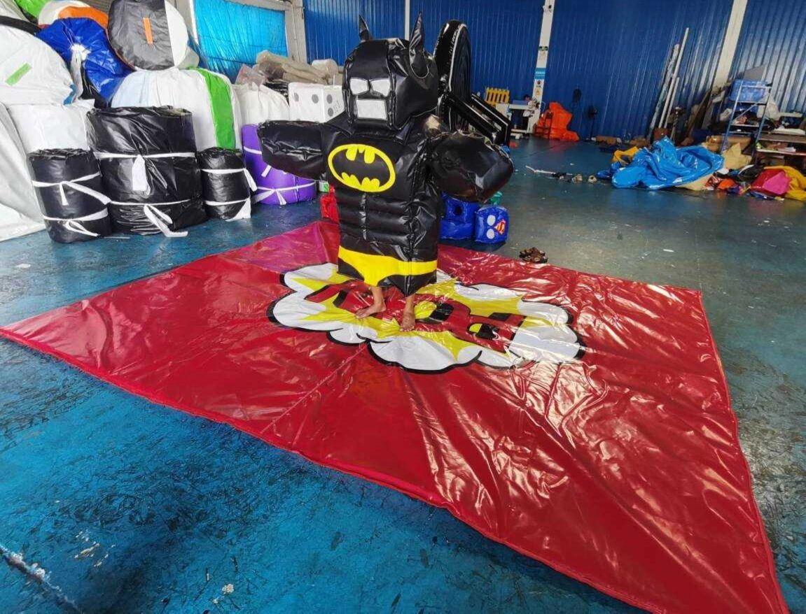 Person in inflatable Batman costume standing on red mat indoors.