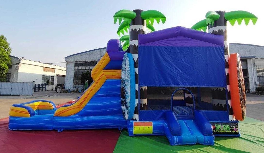 Colorful inflatable bounce house with slide and palm tree decorations.