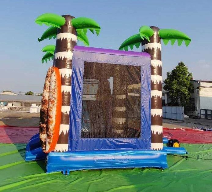 Inflatable bounce house with palm trees and surfboard design outdoors.