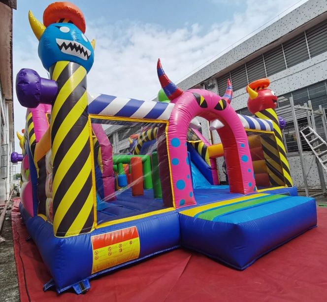 Colorful inflatable bounce house with monster designs and slide outdoors.