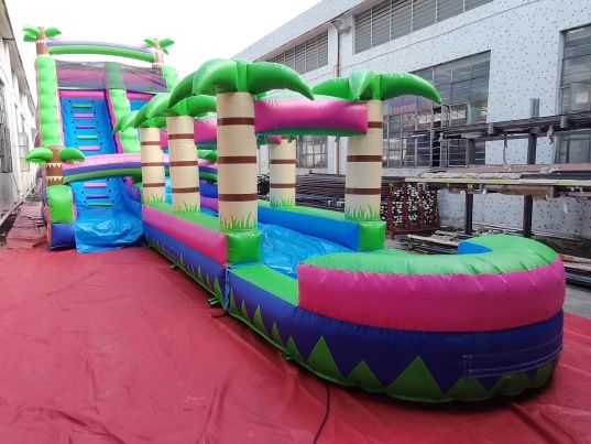 Colorful inflatable water slide with palm tree decorations indoors.