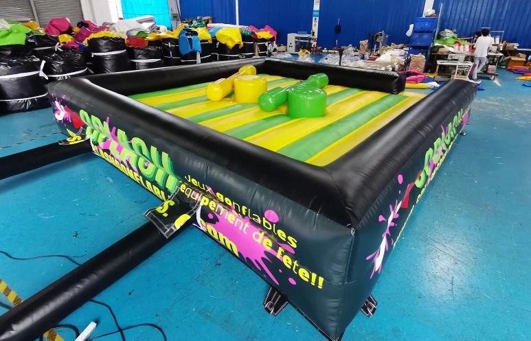 Large inflatable game arena with colorful padded figures on a blue floor indoors.
