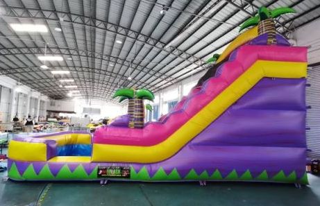 Colorful inflatable slide with palm tree decorations inside a warehouse.