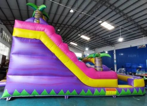 Large colorful inflatable slide with palm tree decorations indoors.