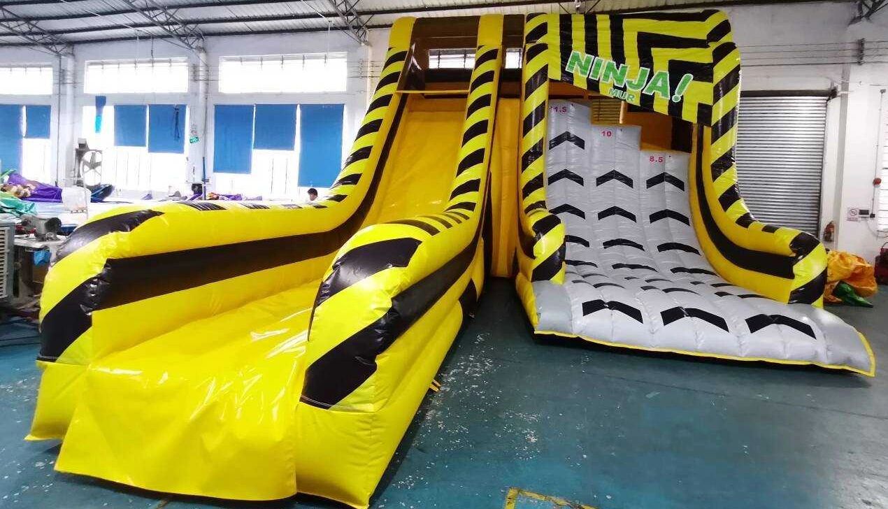 Yellow inflatable ninja-themed slide and climbing wall inside a warehouse.