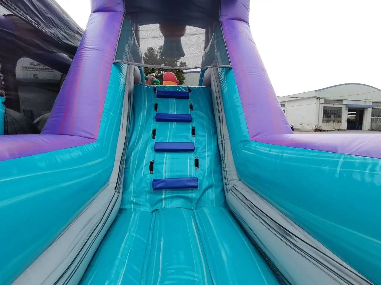 Inflatable blue and purple slide with climbing steps outdoors.