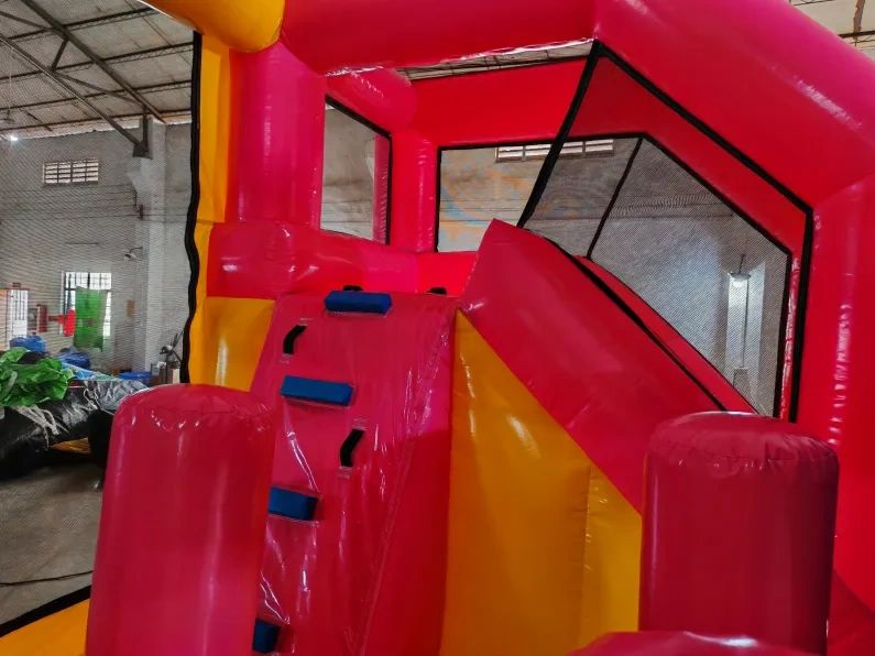 Bright red and yellow inflatable bounce house with slide inside a warehouse.