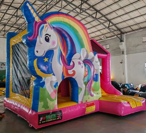 Colorful unicorn-themed inflatable bounce house with a slide indoors.