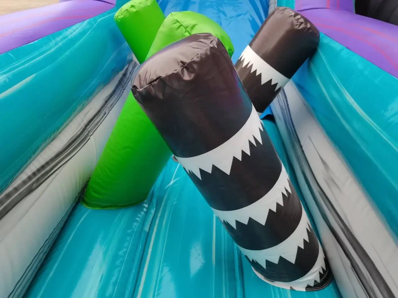 Colorful inflatable obstacle with black and green pillars inside a blue slide.
