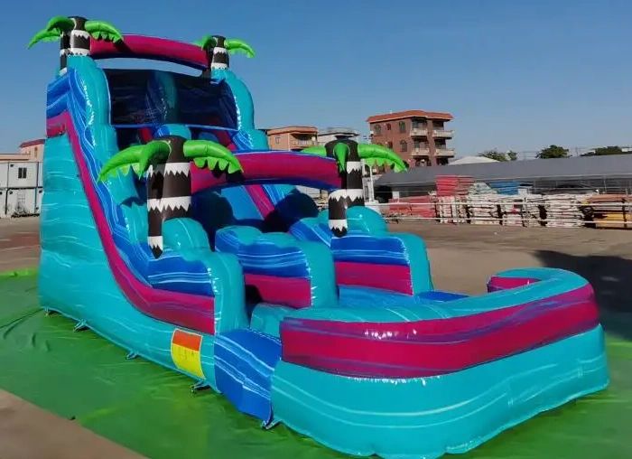 Colorful inflatable water slide with palm tree decorations outdoors.