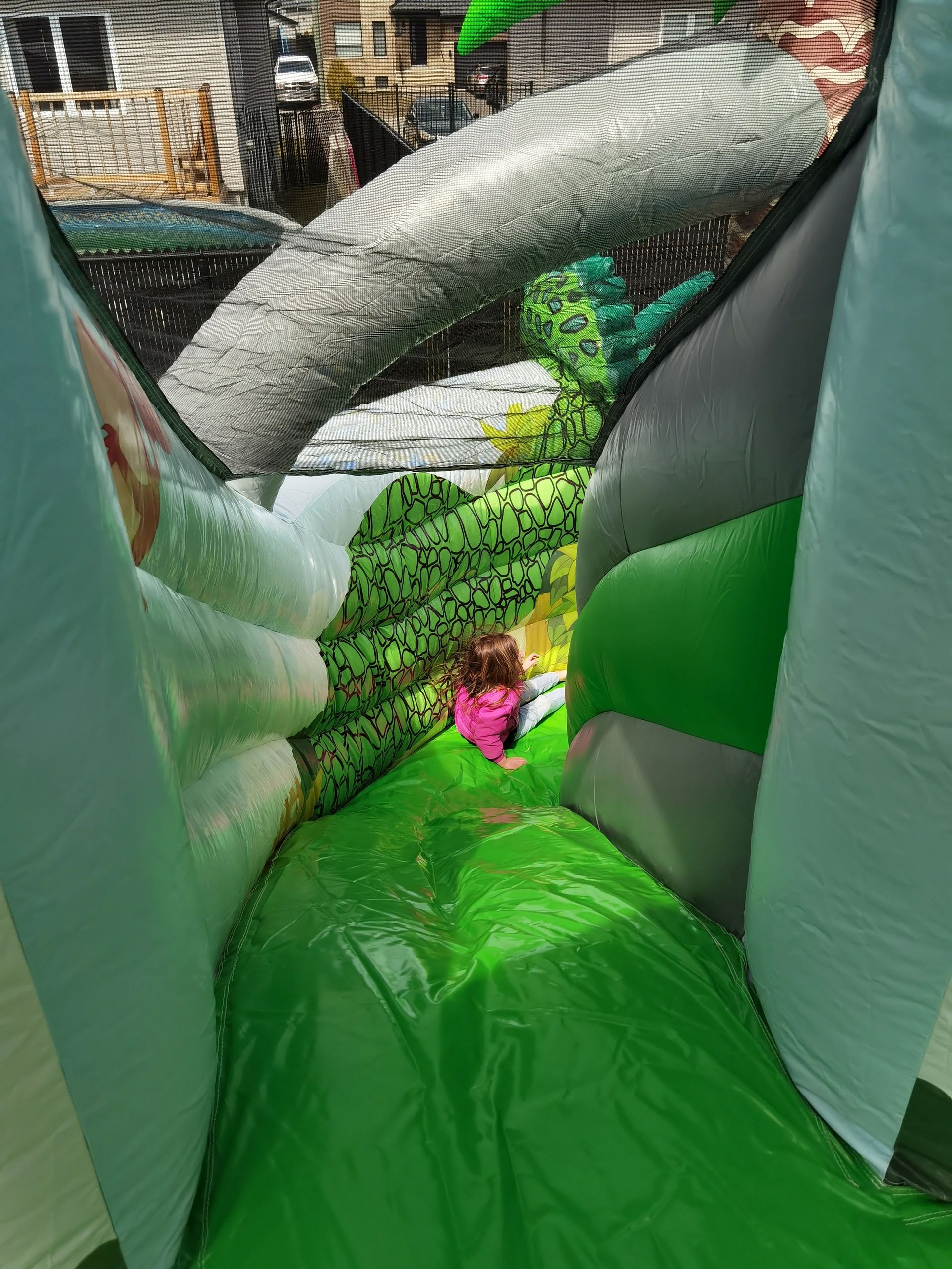 Child playing inside a green dinosaur-themed inflatable slide.