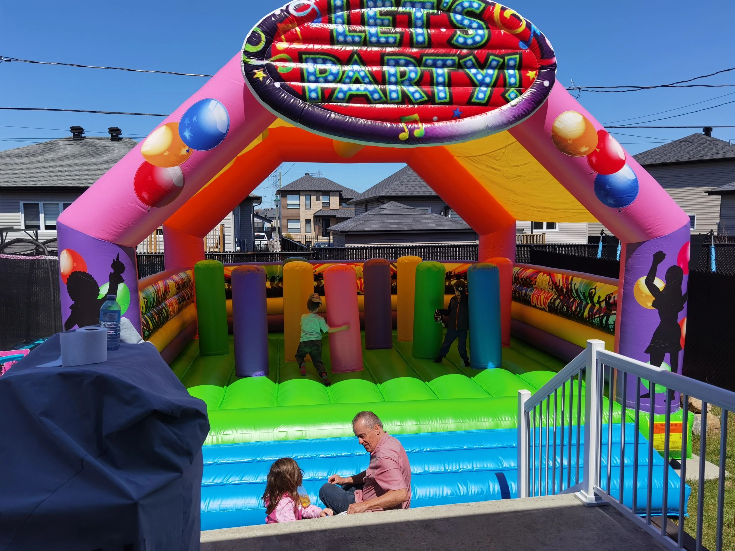 Kids play inside a colorful inflatable bounce house at a sunny party.