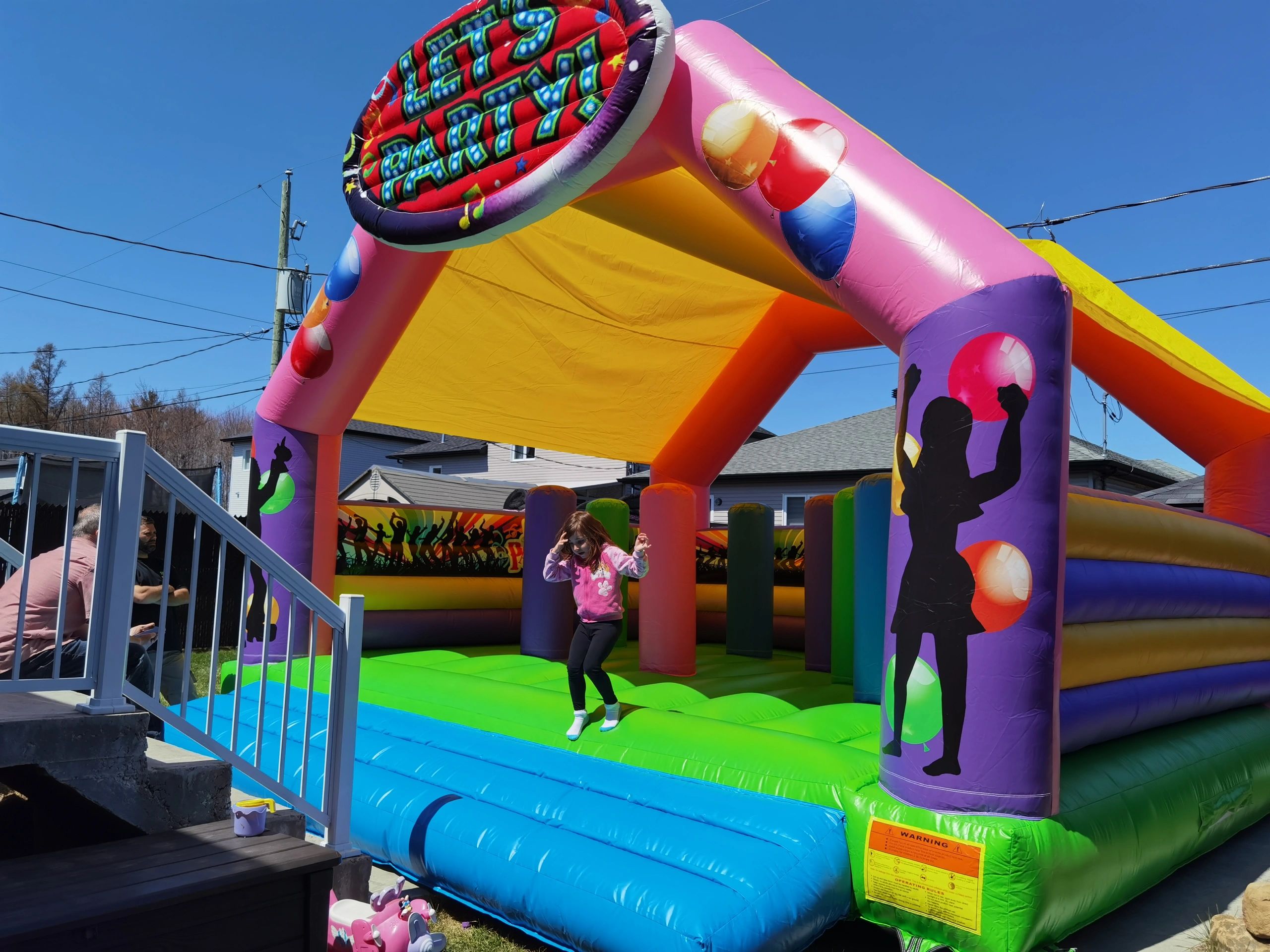 A child enjoys bouncing inside a colorful inflatable bounce house under a clear blue sky.