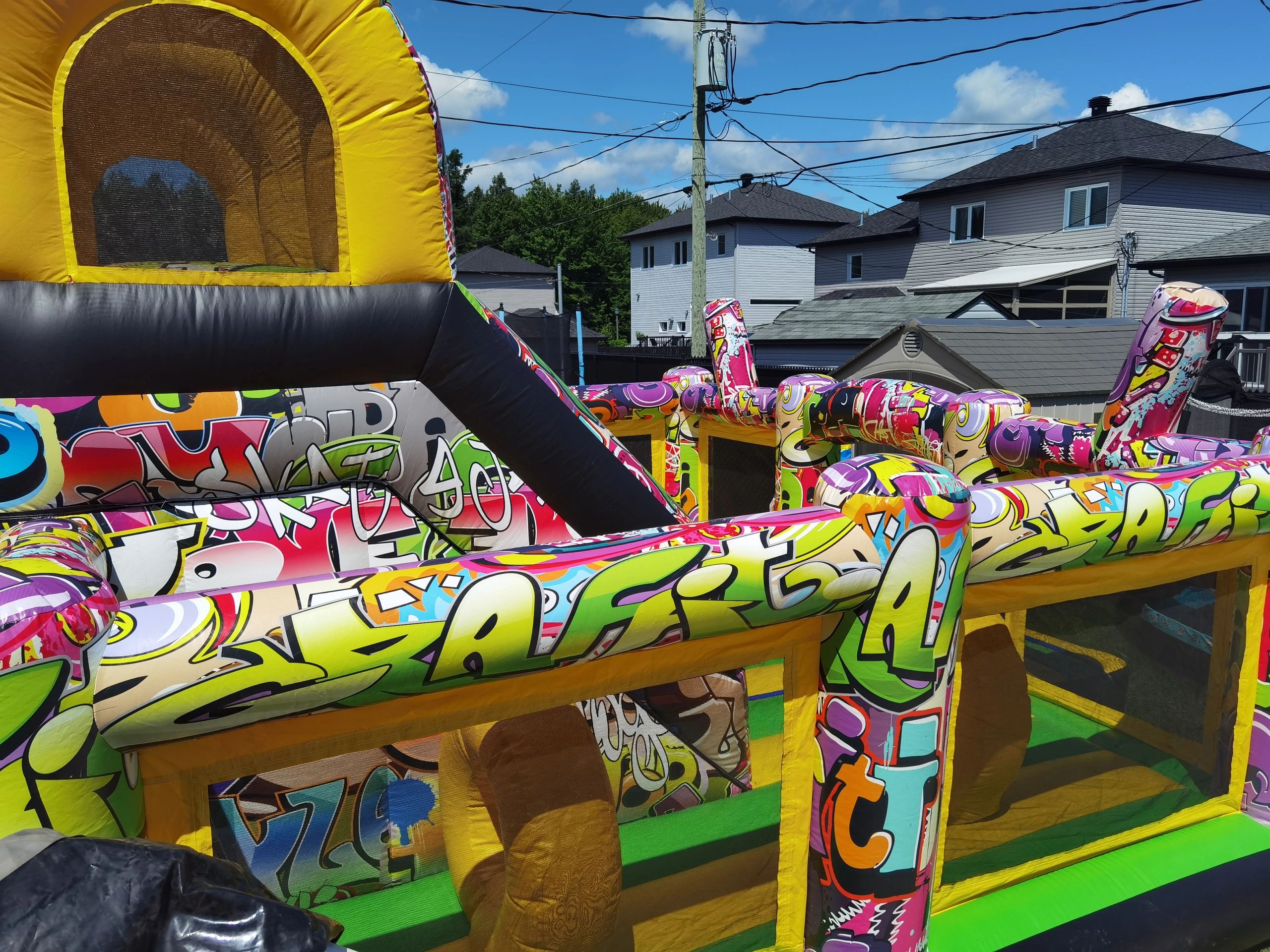 Colorful graffiti-style inflatable bounce house under a sunny blue sky.