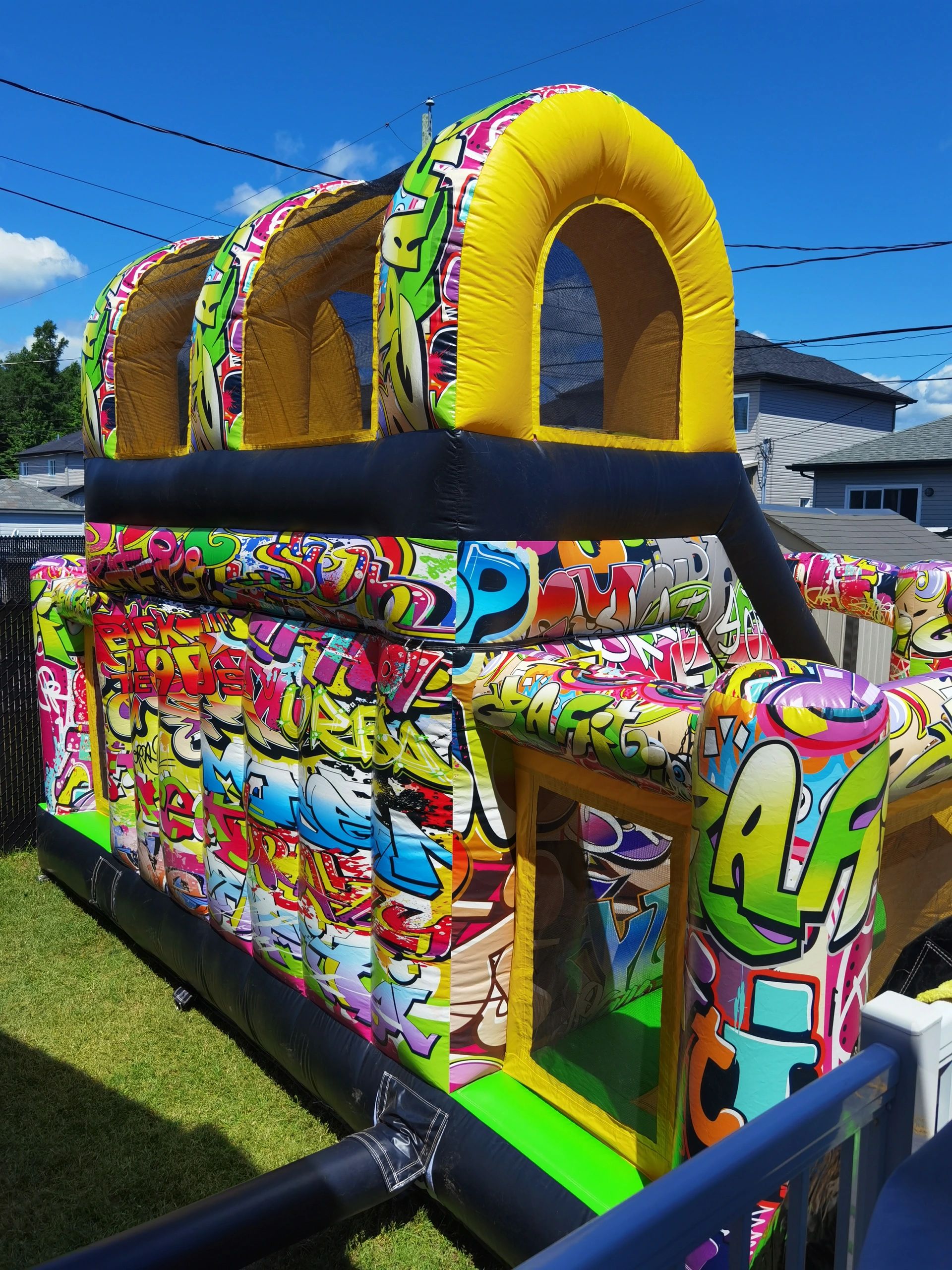 Colorful graffiti-themed inflatable bounce house outdoors on a sunny day.