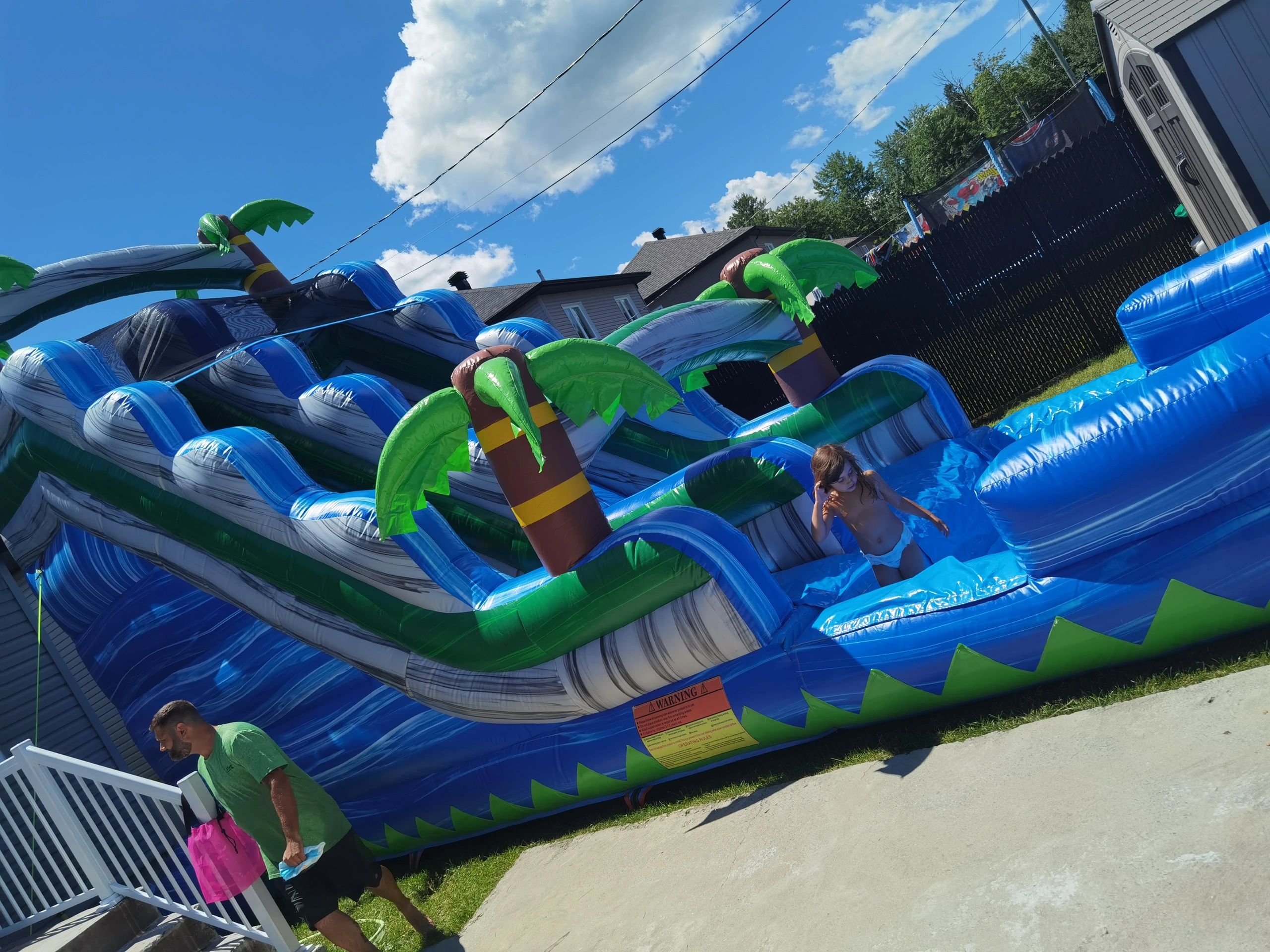 A child enjoys a large inflatable water slide with palm tree designs on a sunny day.