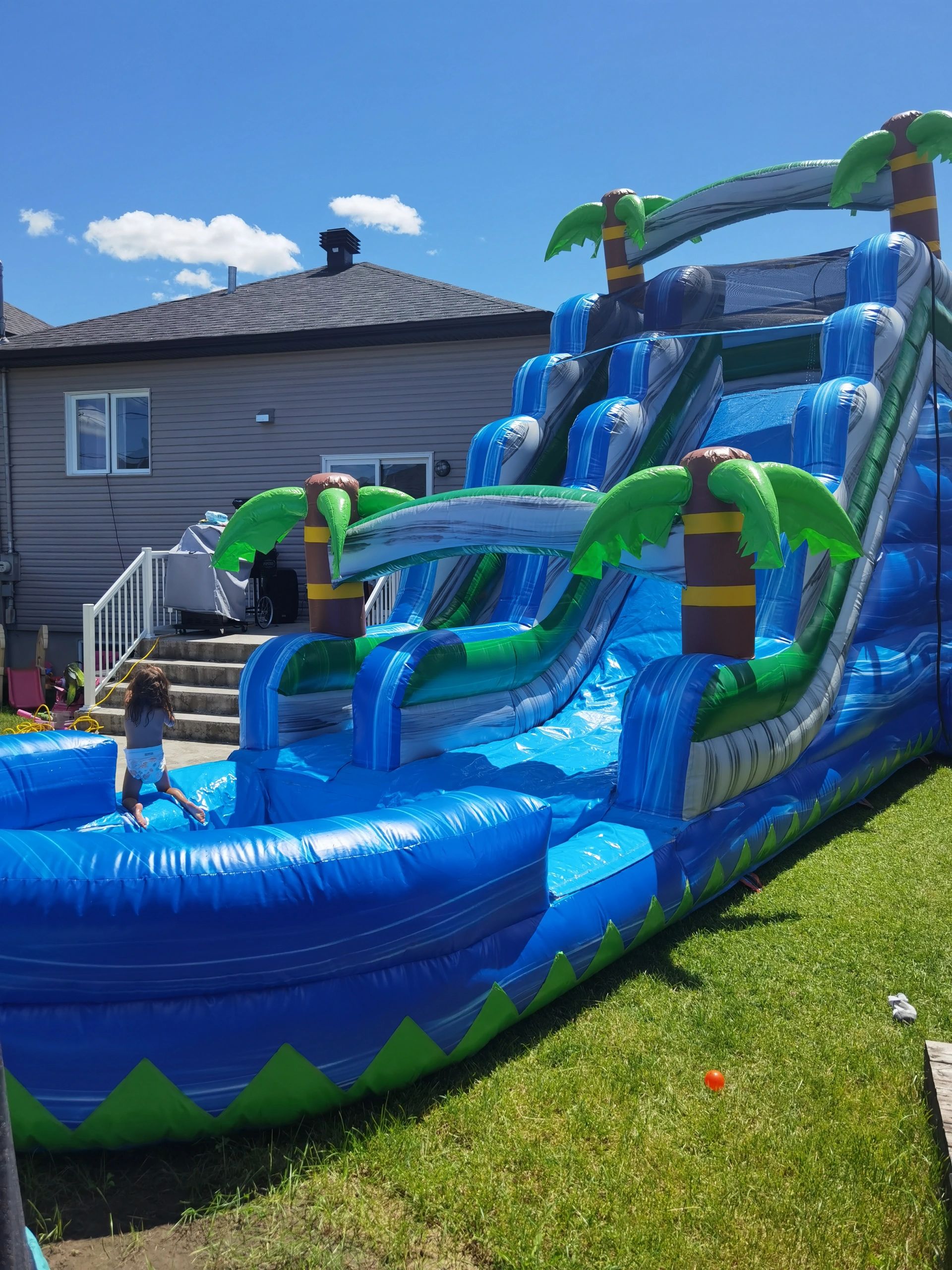 Child playing on a large inflatable water slide in a backyard.