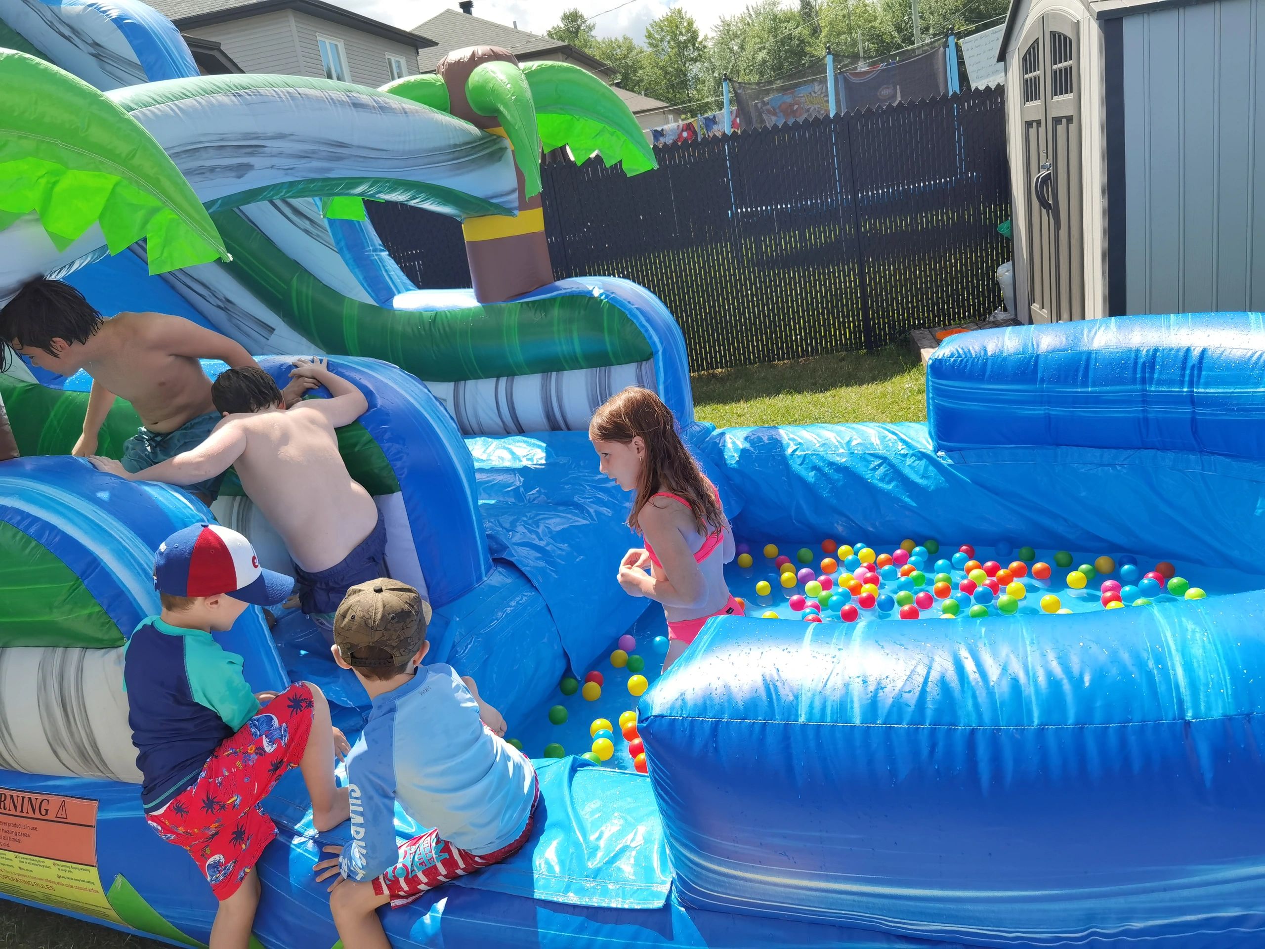 Children playing on a colorful inflatable water slide with plastic balls.