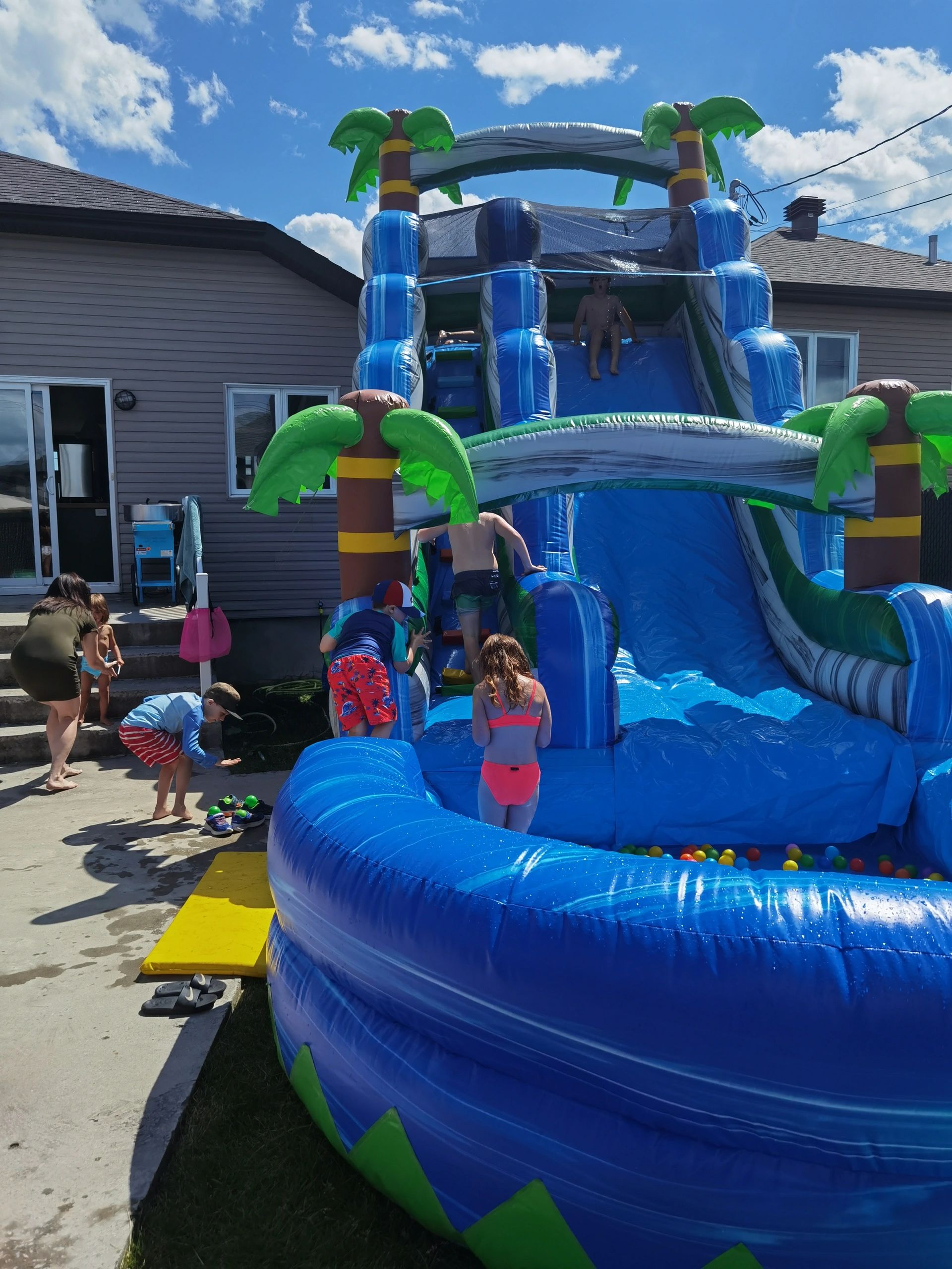 Children playing on a blue inflatable water slide on a sunny day.