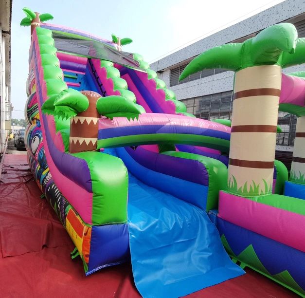 Colorful inflatable slide with palm tree decorations on a red mat outdoors.