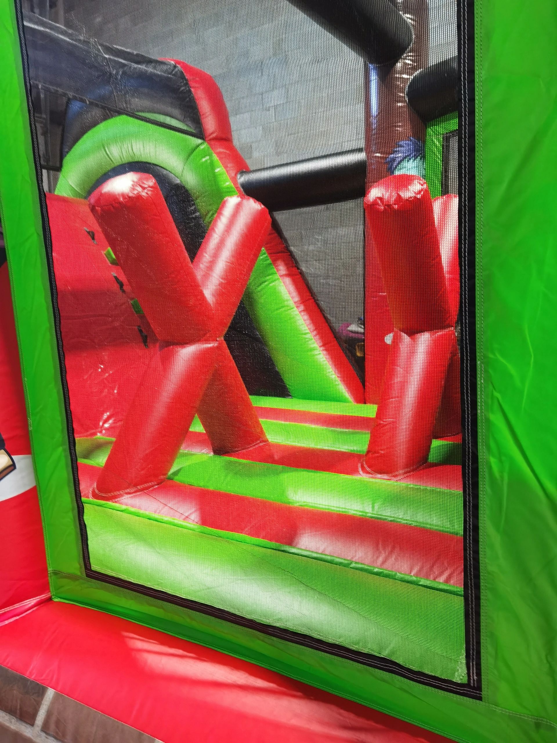 Colorful inflatable obstacle course with red, green, and black elements seen through a mesh.