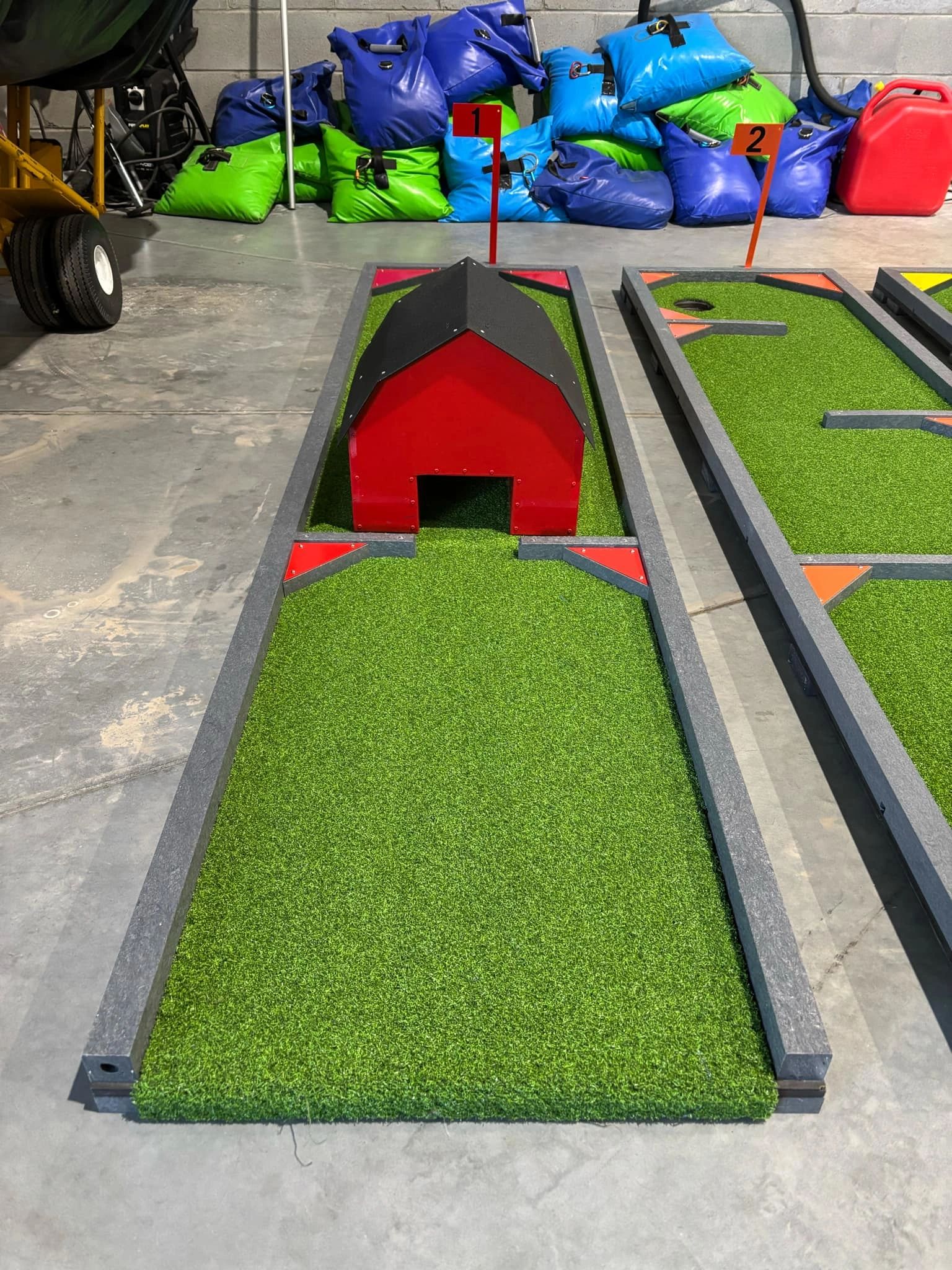 Indoor mini golf hole with red barn obstacle and numbered flags.