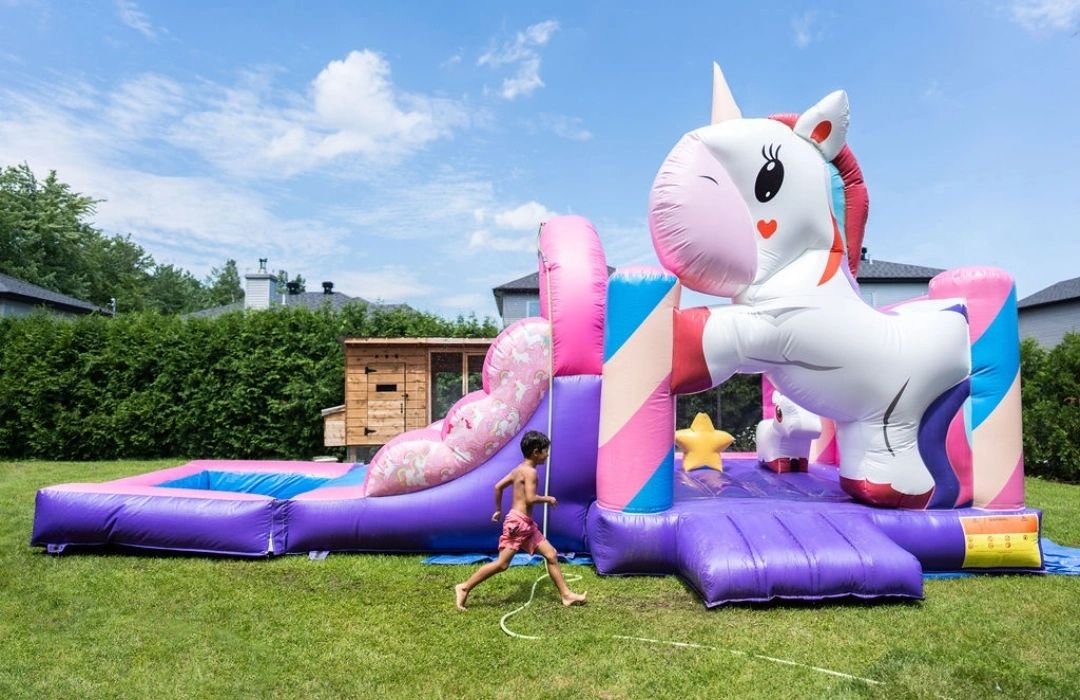 A child runs past a colorful unicorn-themed inflatable bounce house on a sunny day.