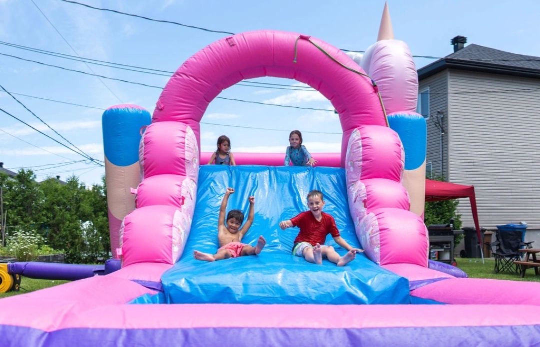 Children enjoying a colorful inflatable water slide in a backyard.