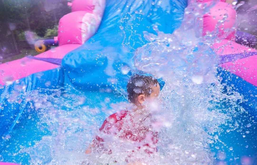 Child splashing into water at the bottom of a colorful inflatable slide.