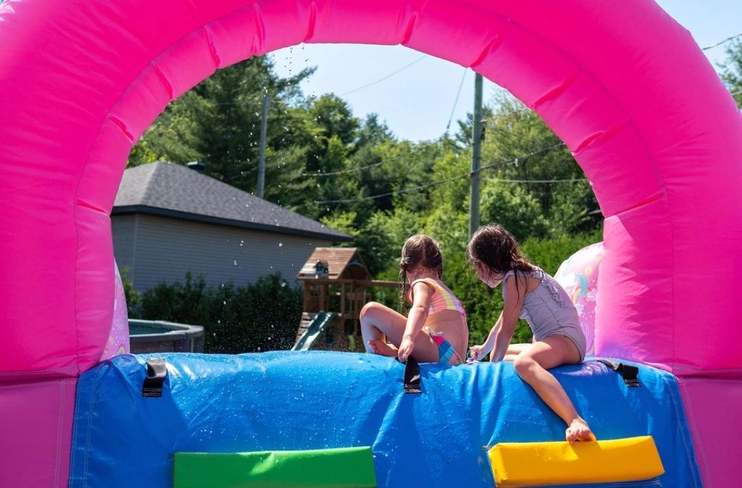 Two children playing on a colorful inflatable water slide on a sunny day.