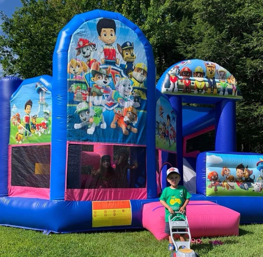 Child playing outside a colorful Paw Patrol-themed bounce house on a sunny day.