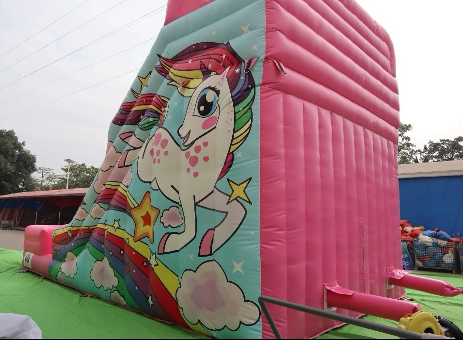 Pink inflatable with a colorful unicorn and rainbow design outdoors.