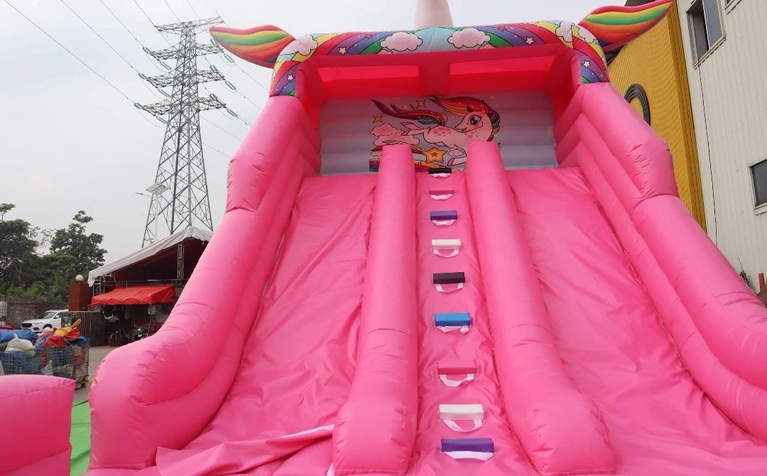 Large pink inflatable unicorn-themed slide with rainbow and clouds design.