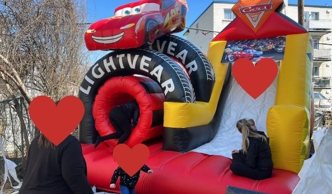 Kids playing on a Cars-themed inflatable slide outdoors.