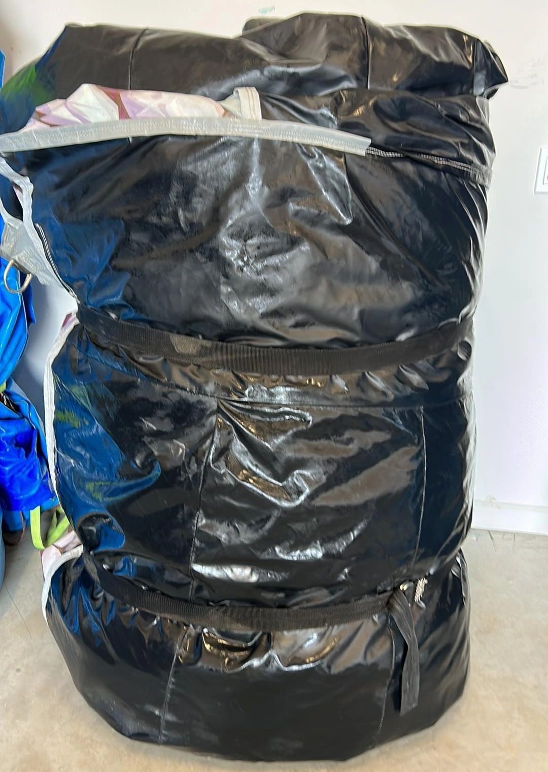 Large black shiny bag filled with items, placed indoors.