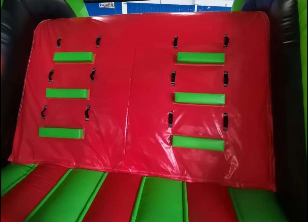 Red and green padded climbing wall with hand grips inside an inflatable play structure.