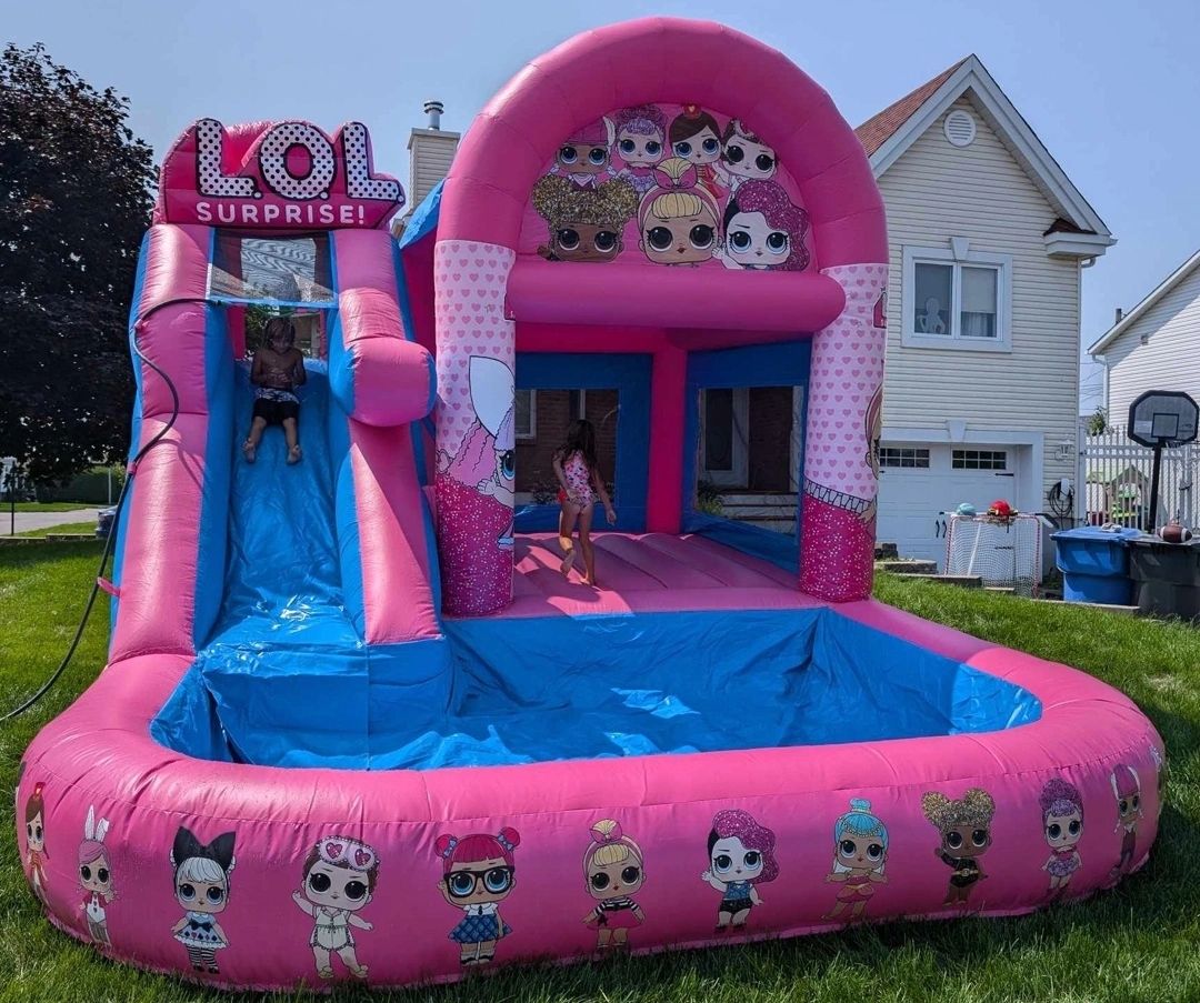 Children playing on a pink LOL Surprise inflatable water slide in a backyard.