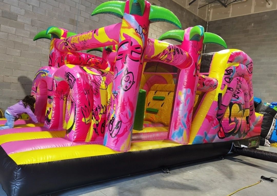A vibrant pink and yellow inflatable bounce house with graffiti designs indoors.