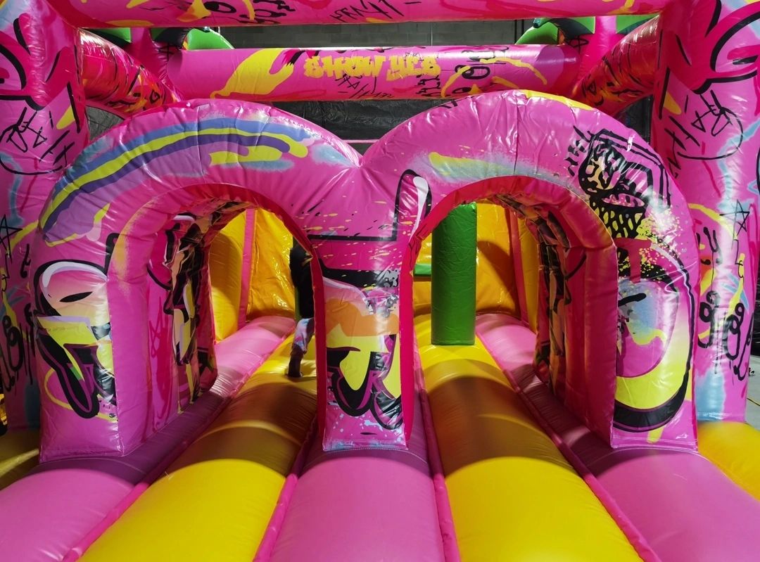 Colorful inflatable obstacle course with pink and yellow arches and graffiti designs.