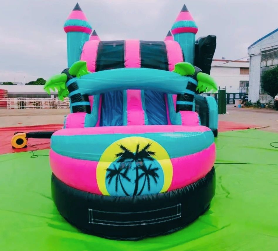 Colorful inflatable bounce house with palm tree design on a green mat.