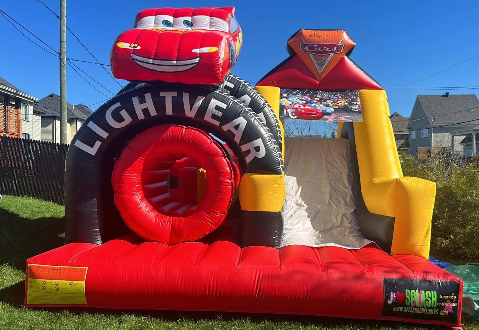 Inflatable bounce house with Cars 2 theme featuring Lightning McQueen under a clear blue sky.