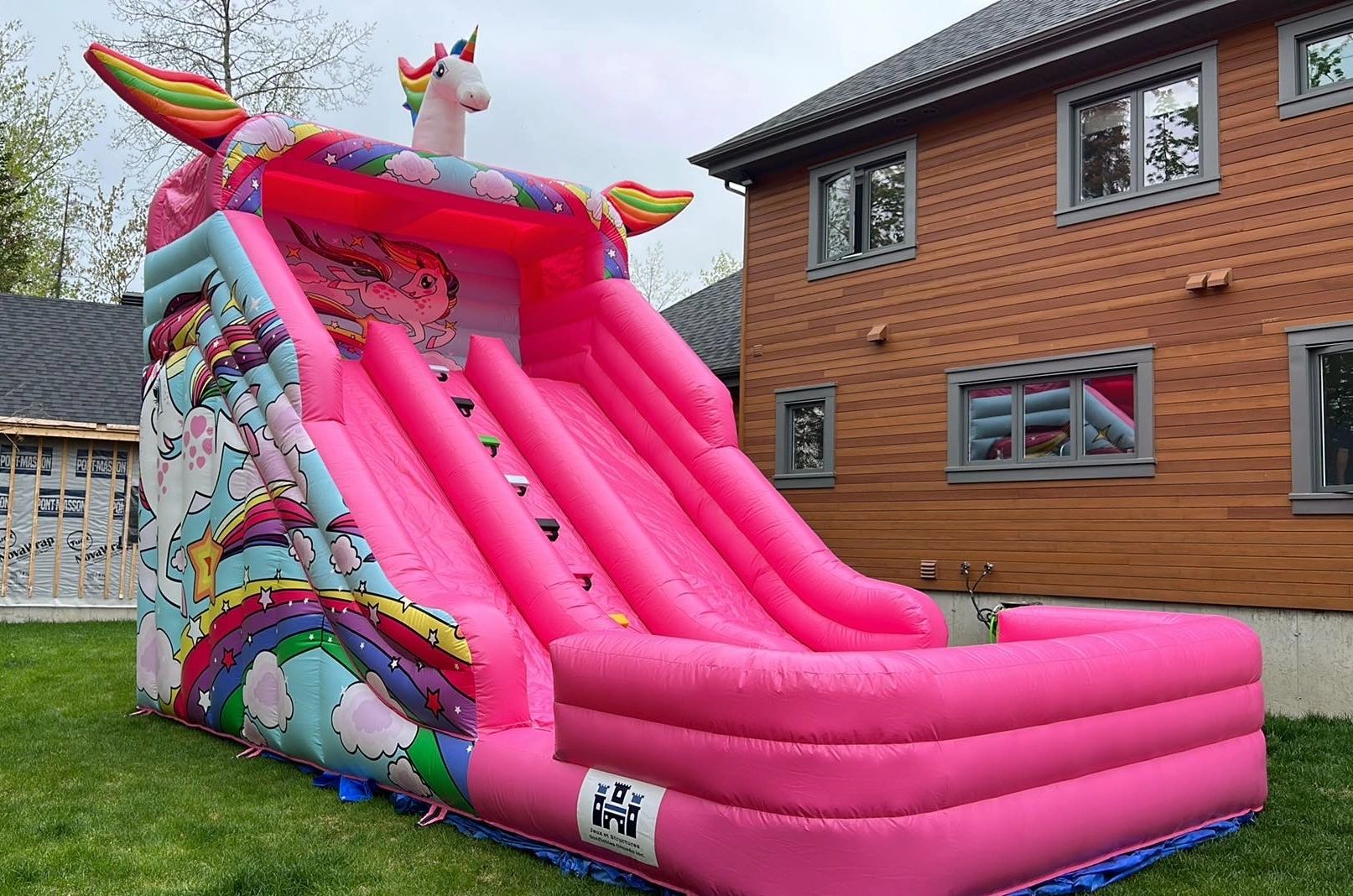Bright pink inflatable unicorn slide in a backyard.