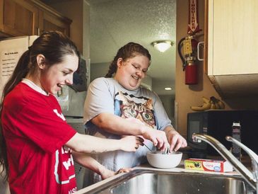 Two young people happily preparing food together in a kitchen.