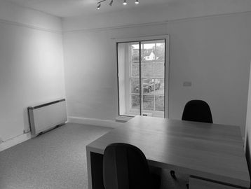 Small office with a wooden desk and two chairs by a window.