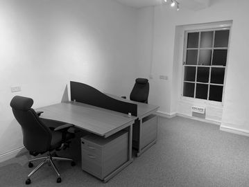 Minimalist office with two desks and chairs by a window.