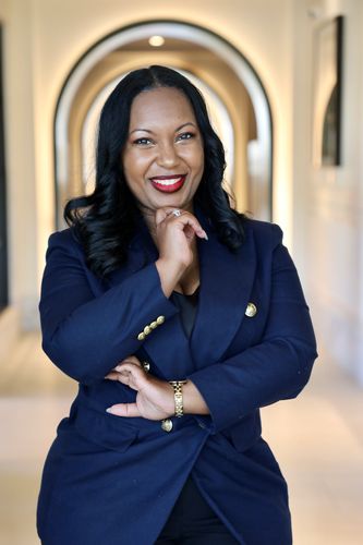 Confident woman in navy blazer smiling brightly in an elegant hallway.