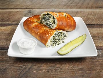 Savory stuffed pastry with dipping sauce and pickle spear.