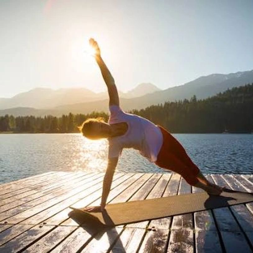 Person doing side plank yoga on a dock by the lake at sunrise.